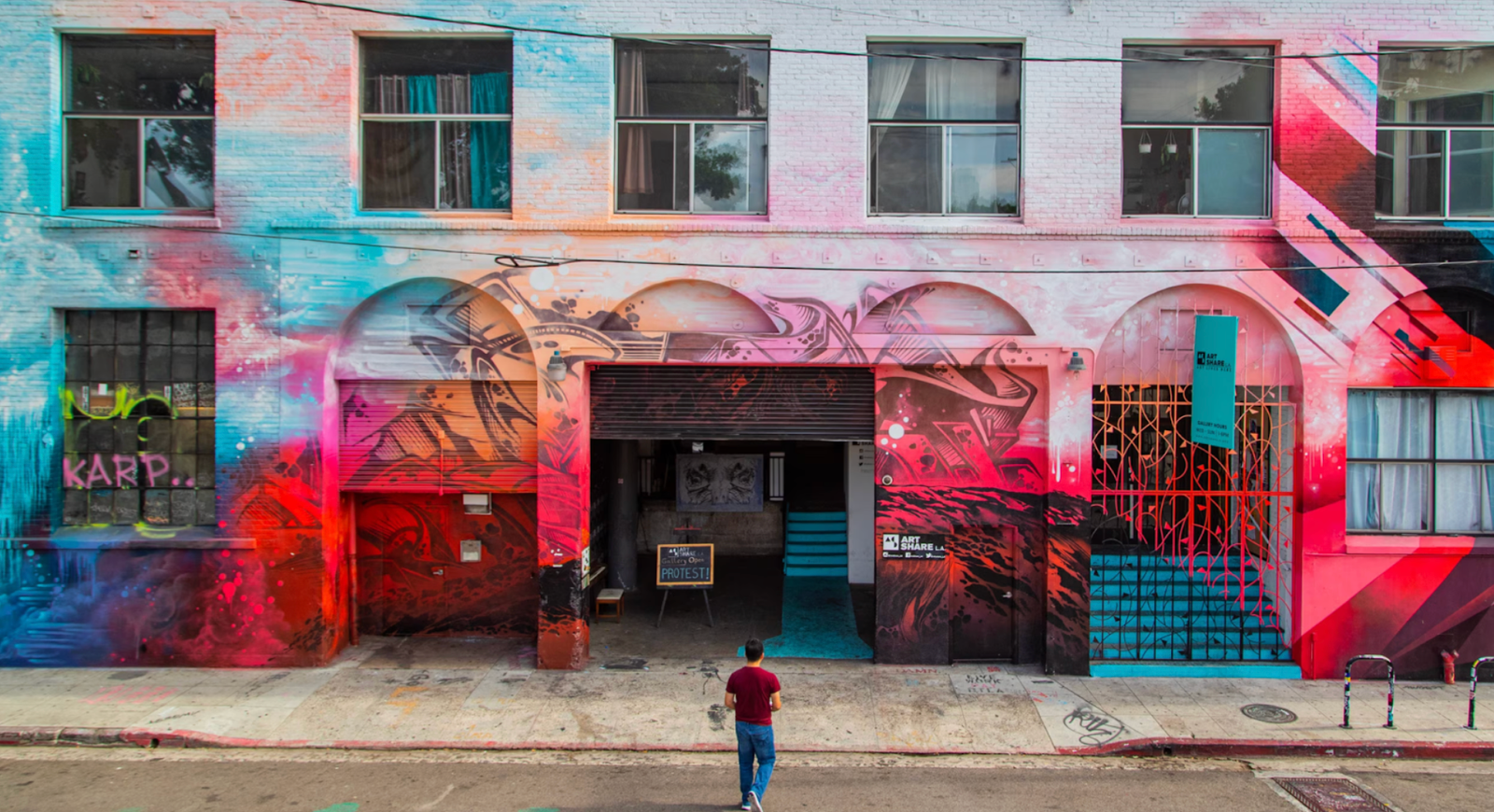 A person strolls past a vibrant building covered in colorful graffiti art.